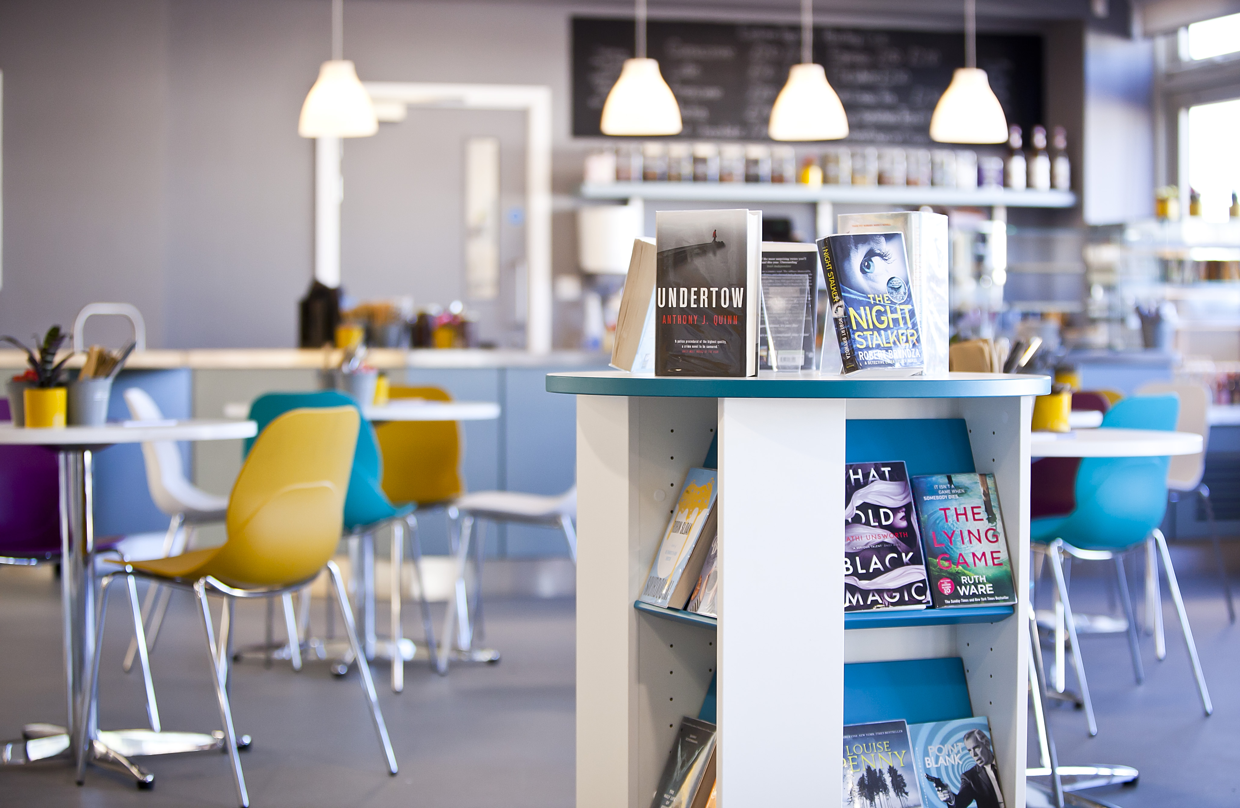 The cafe at Burnholme, showing seating around tables, and a book display unit