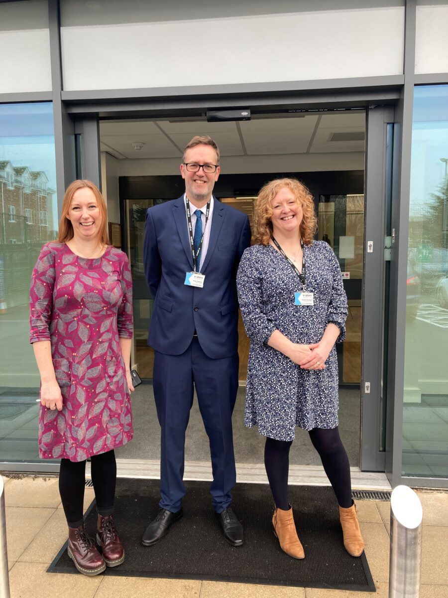 Lisa Wellington (Community Centre Manager) Andy Stanton and Sarah Garbacz (both from Explore) stand in front of the building. Lisa wears a magenta dress patterned with leaves, Andy a blue suit and tie and Sarah a blue and white patterned dress.