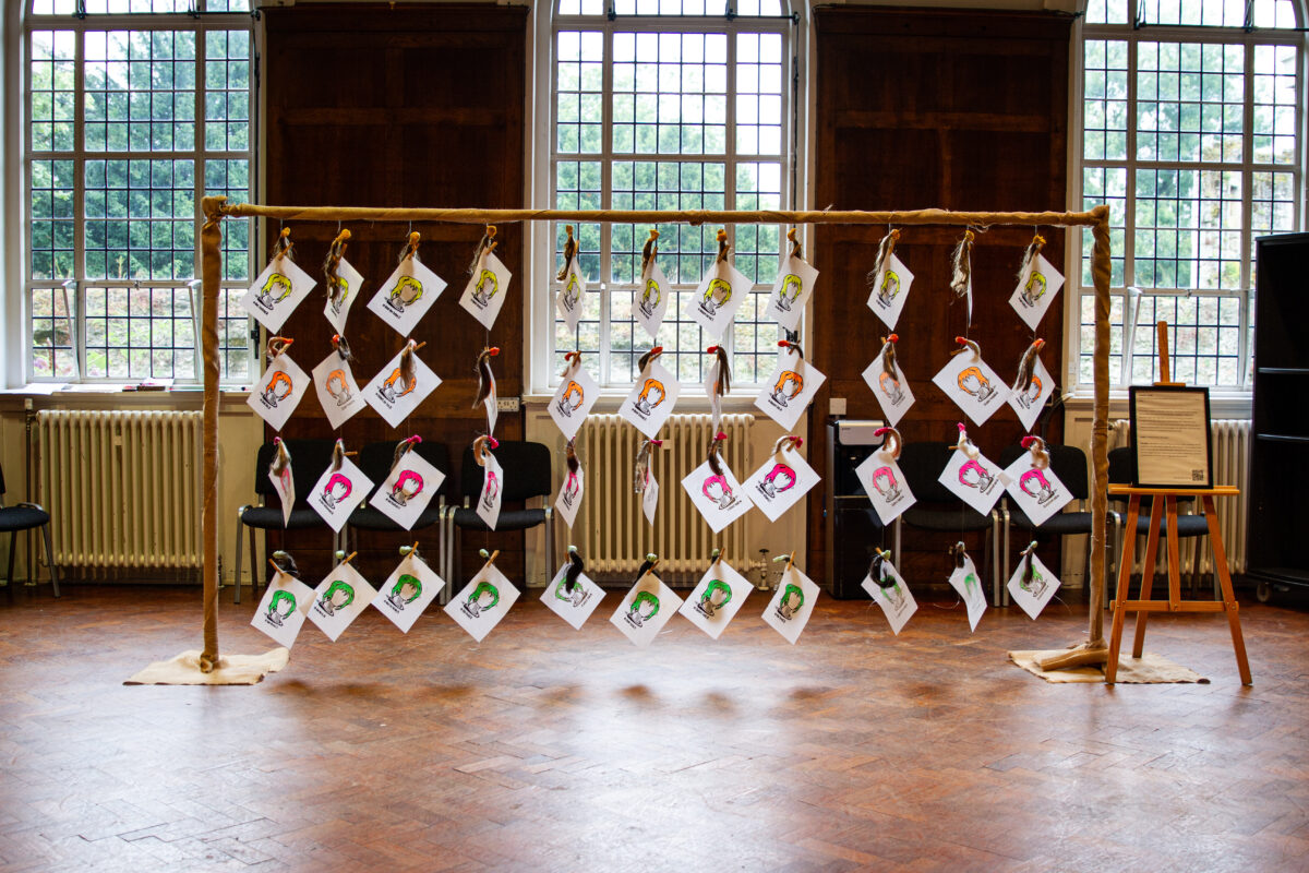 A wooden frame holding multiple small artworks depicting colorful portraits, hung in a large room with wooden paneling and large windows.