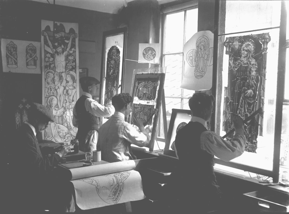 A group of people working on stained glass panels in a room