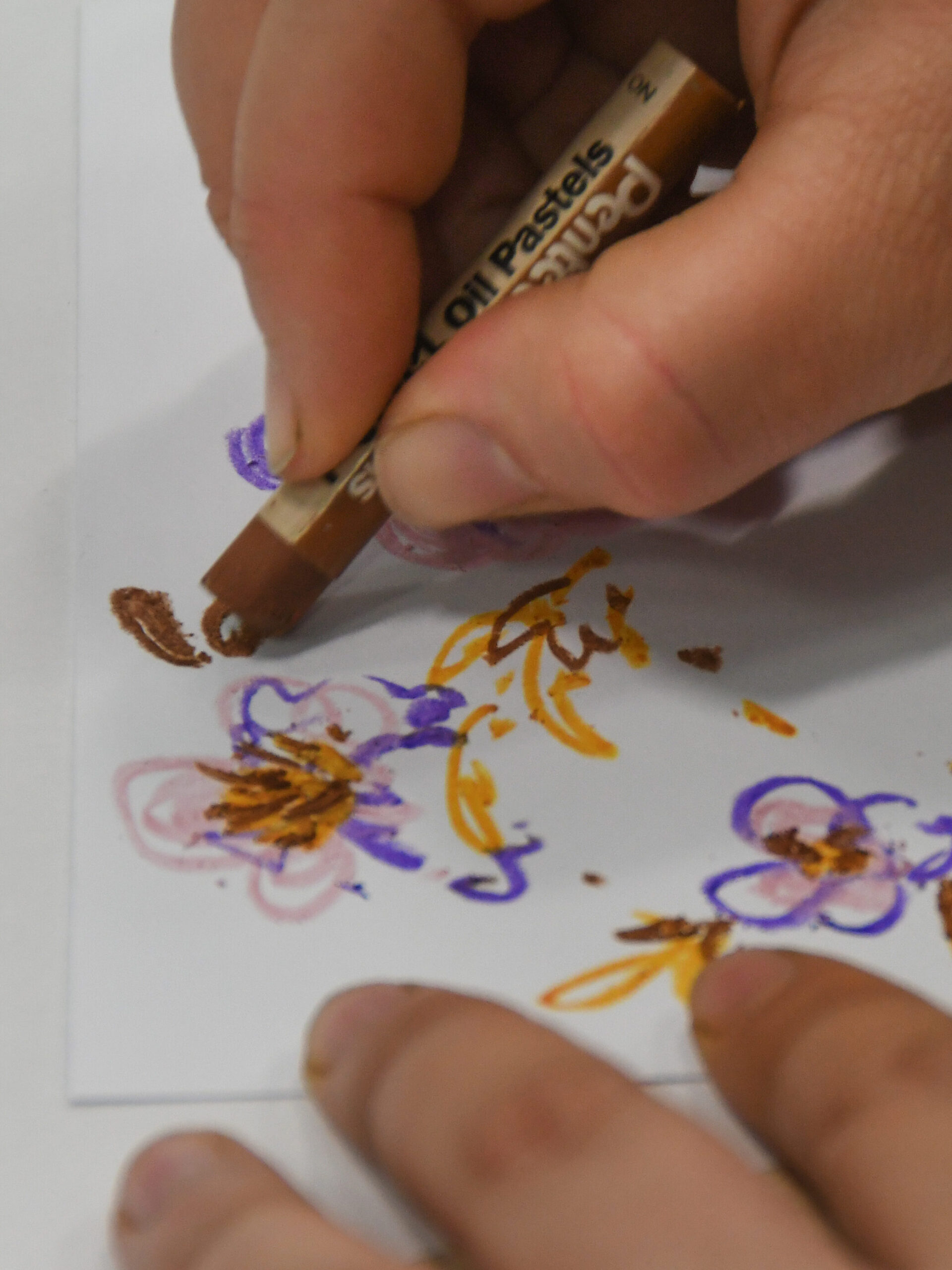 A hand using an oil pastel crayon to draw.