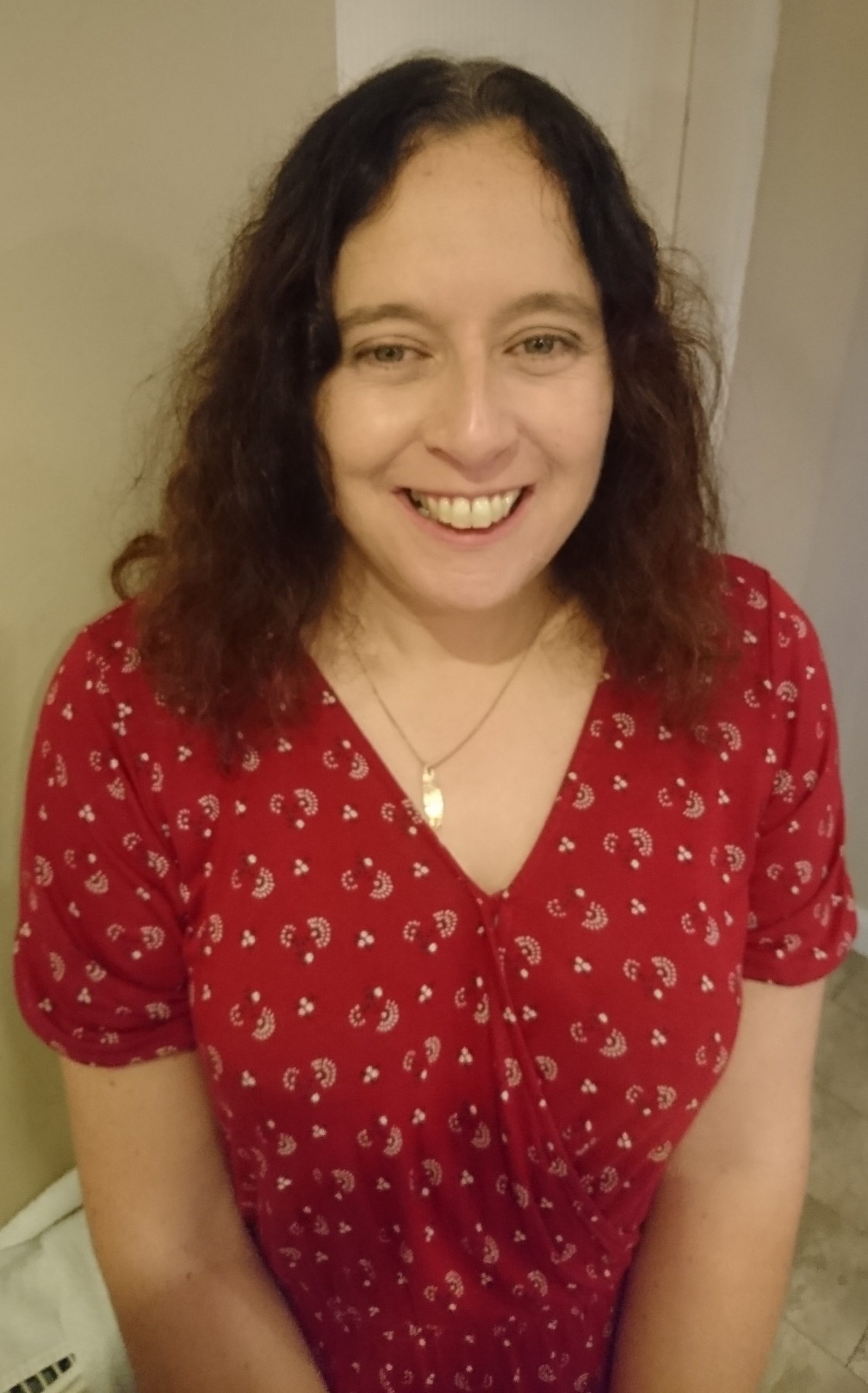 Fiona has long brown hair and is wearing a red dress. She is smiling.