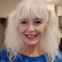 Lee has white hair with a fringe and is smiling.